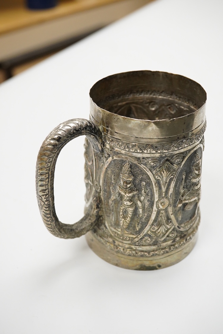 A 19th Century Indian white metal mug, embossed with deities, 11.1cm.